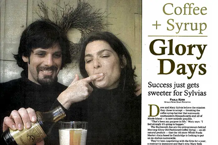 A magazine or newspaper-style page with a photo of owners on the left and a large headline reading 'Coffee + Syrup Glory Days' on the right. The woman is applying syrup to her mouth, and a bottle is visible at the bottom left.